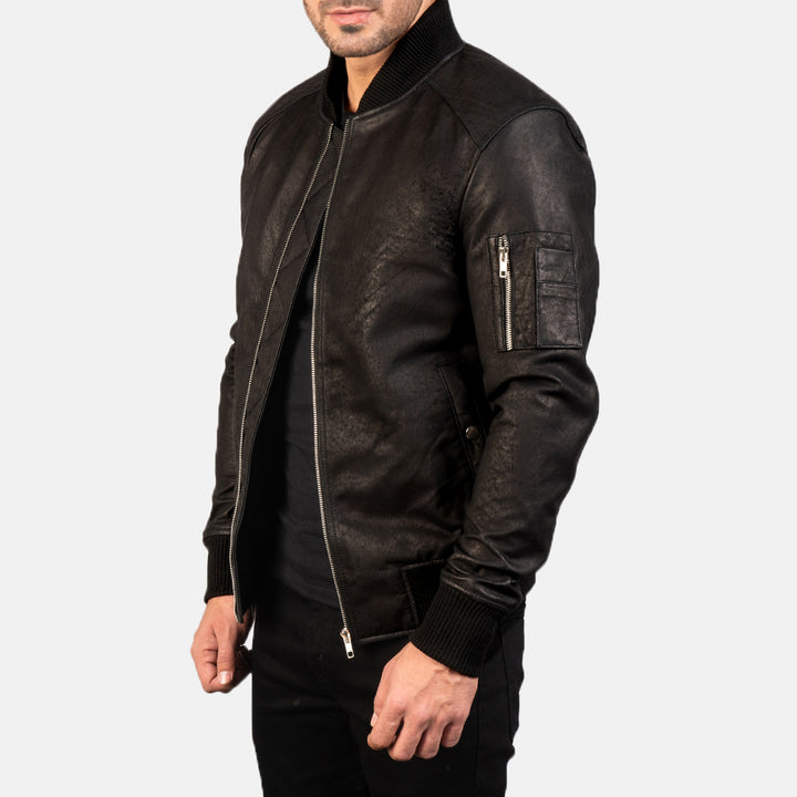  Side view of a male model wearing a Black Bomia Ma-1 Leather Bomber Jacket with a standing collar, zipper closure, and rib knit cuffs, paired with a black t-shirt and black pants.