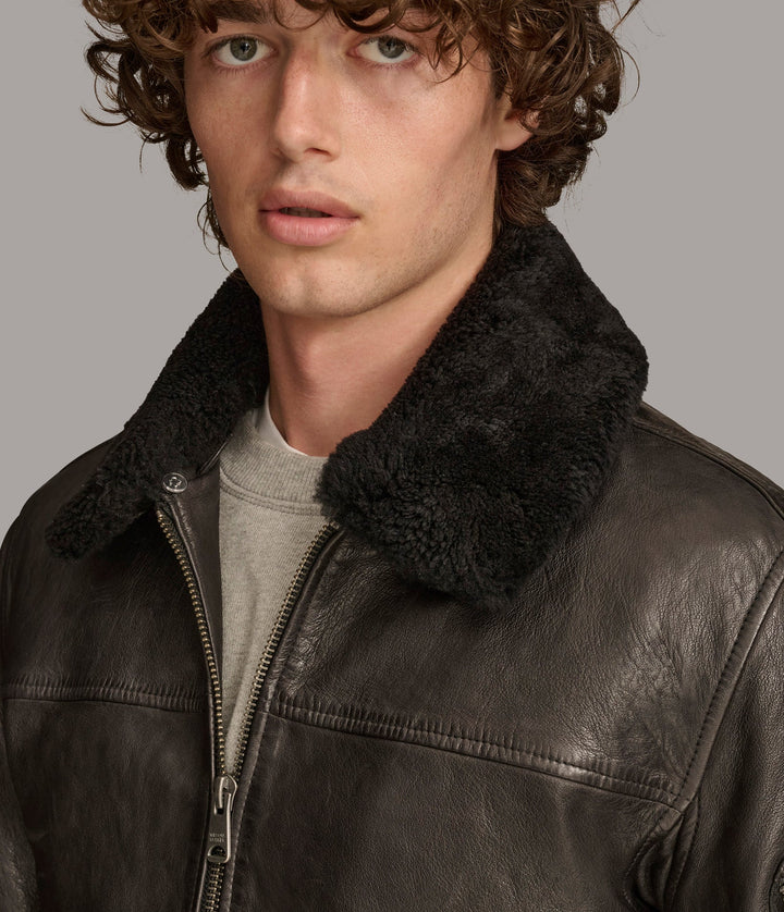 Closeup view of a man wearing Black Ace Bomber Jacket with a fur lining, zipper pockets, and a rib knit collar and closed zipper 