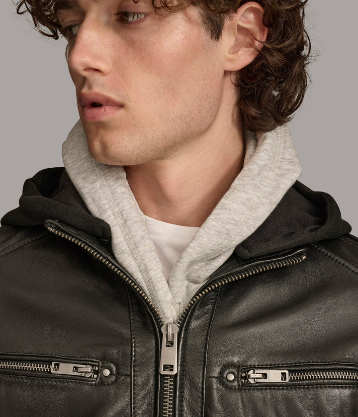 Closeup frontside view of a man wearing a Nico Hooded Racer jacket with a standing collar, zipper pockets, and a detachable fleece hood, paired with blue jeans and closed zipper.